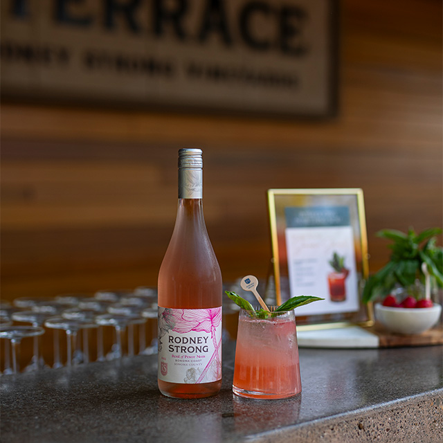 Rosé cocktail and wine bottle on a wooden bar